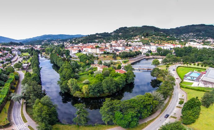A imagem mostra uma vista aérea da vila de Arcos de Valdevez, sobressaindo o verde da vegetação e o azul do rio Vez