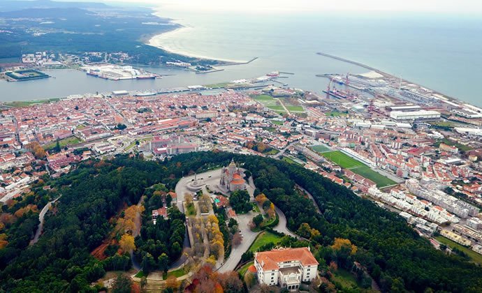 A imagem mostra uma vista aérea da cidade de Viana do Castelo, com o Templo de Santa Luzia, o centro histórico, a foz do rio Lima e a praia do Cabedelo